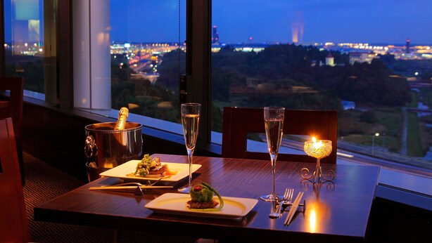 Een eettafel met een champagnefles, twee glazen, een kaars en borden met eten.