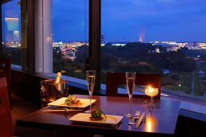 A dining table with a bottle of champagne, two glasses, a candle, and plates of food.