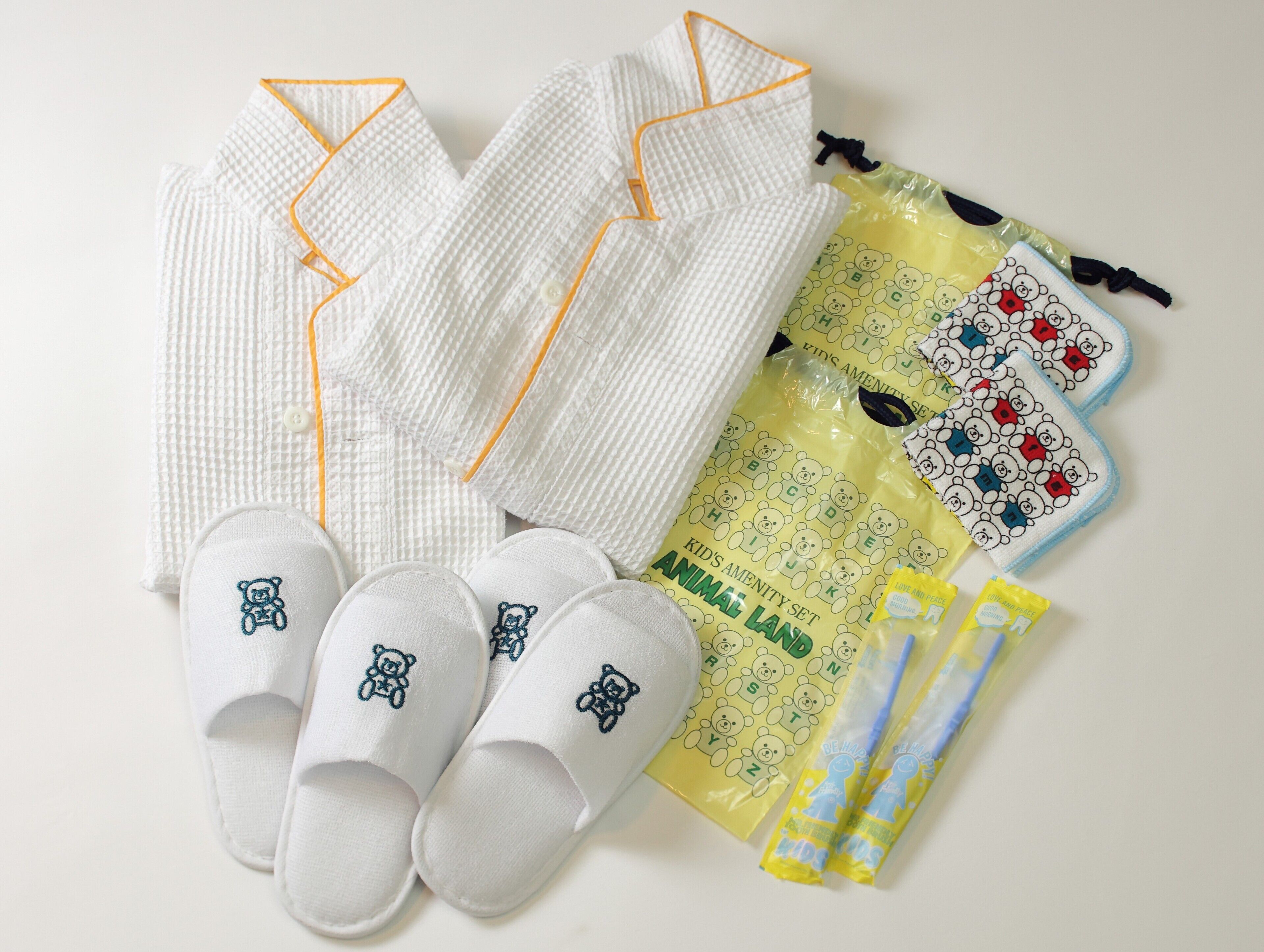 A set of white pajamas with orange trim, a pair of white slippers with bear designs, and a yellow bag with bear patterns.