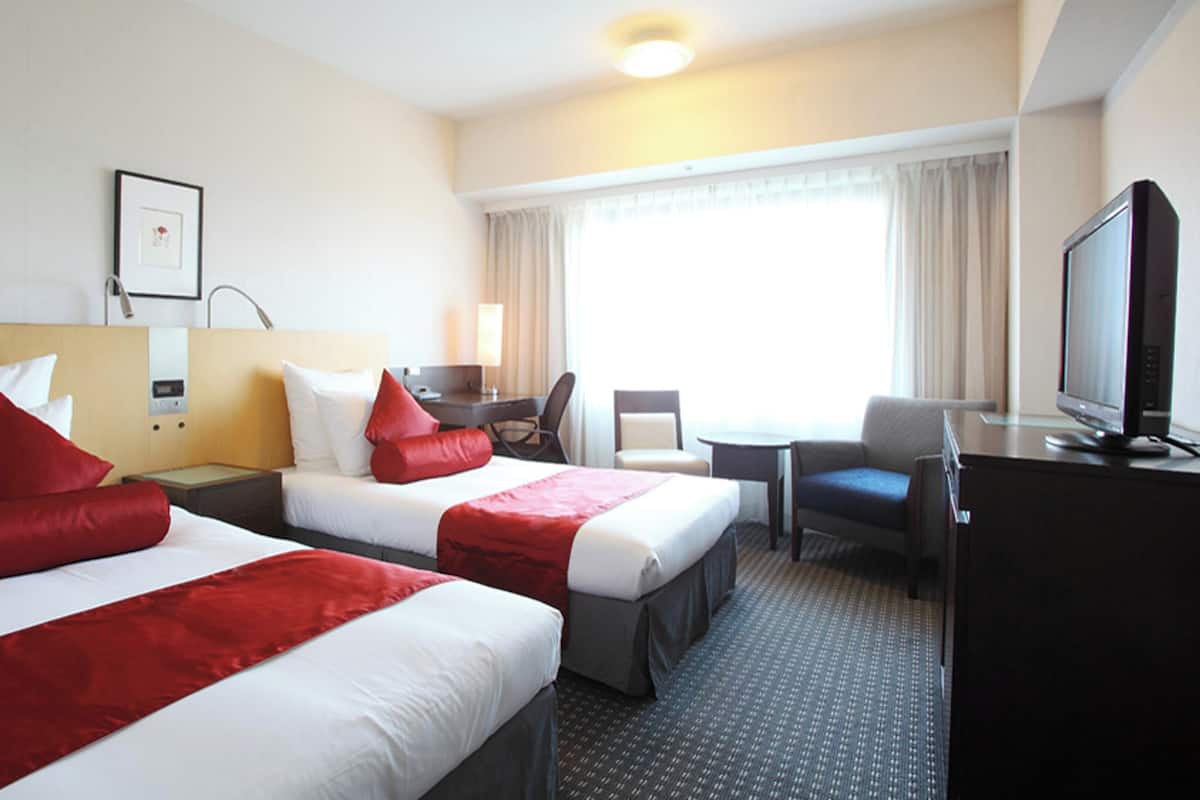 A hotel room with two beds, a desk, a chair, a television, and a window with curtains.