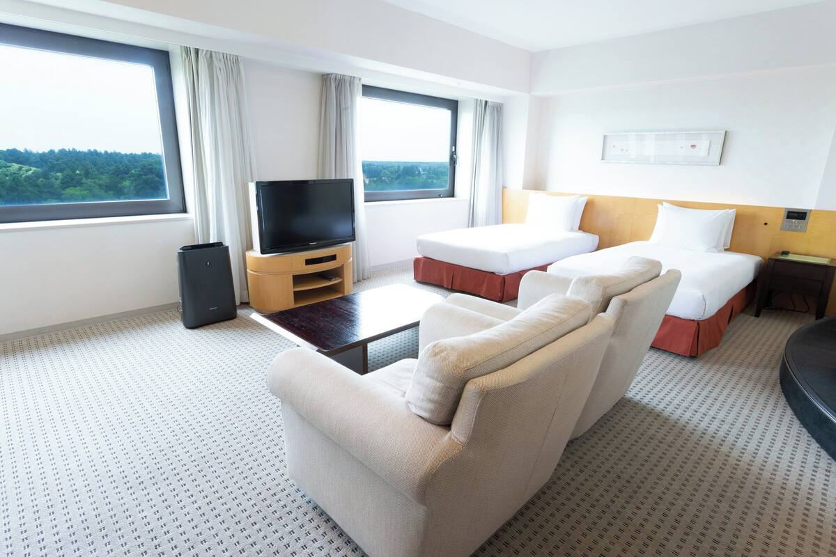 A hotel room with two beds, a sofa, a TV, and a large window with a view.