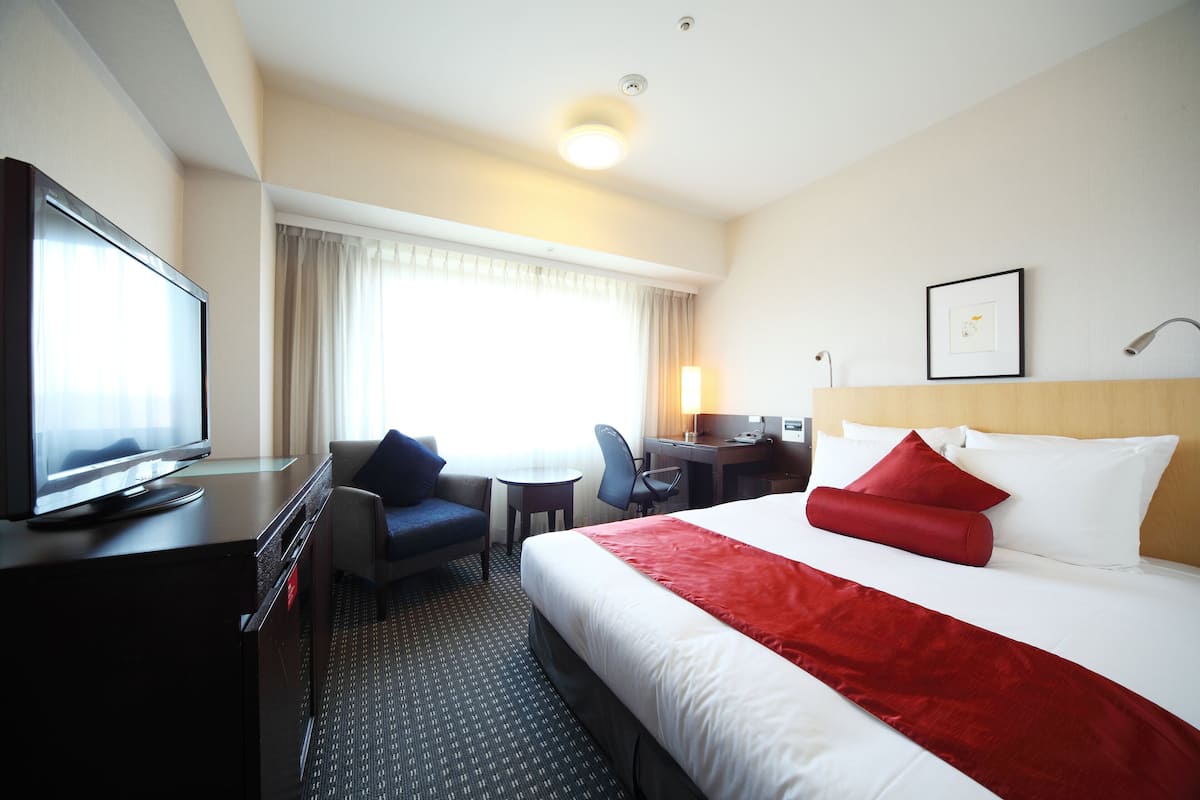 A hotel room with a bed, a desk, a television, a chair, and a window with curtains.