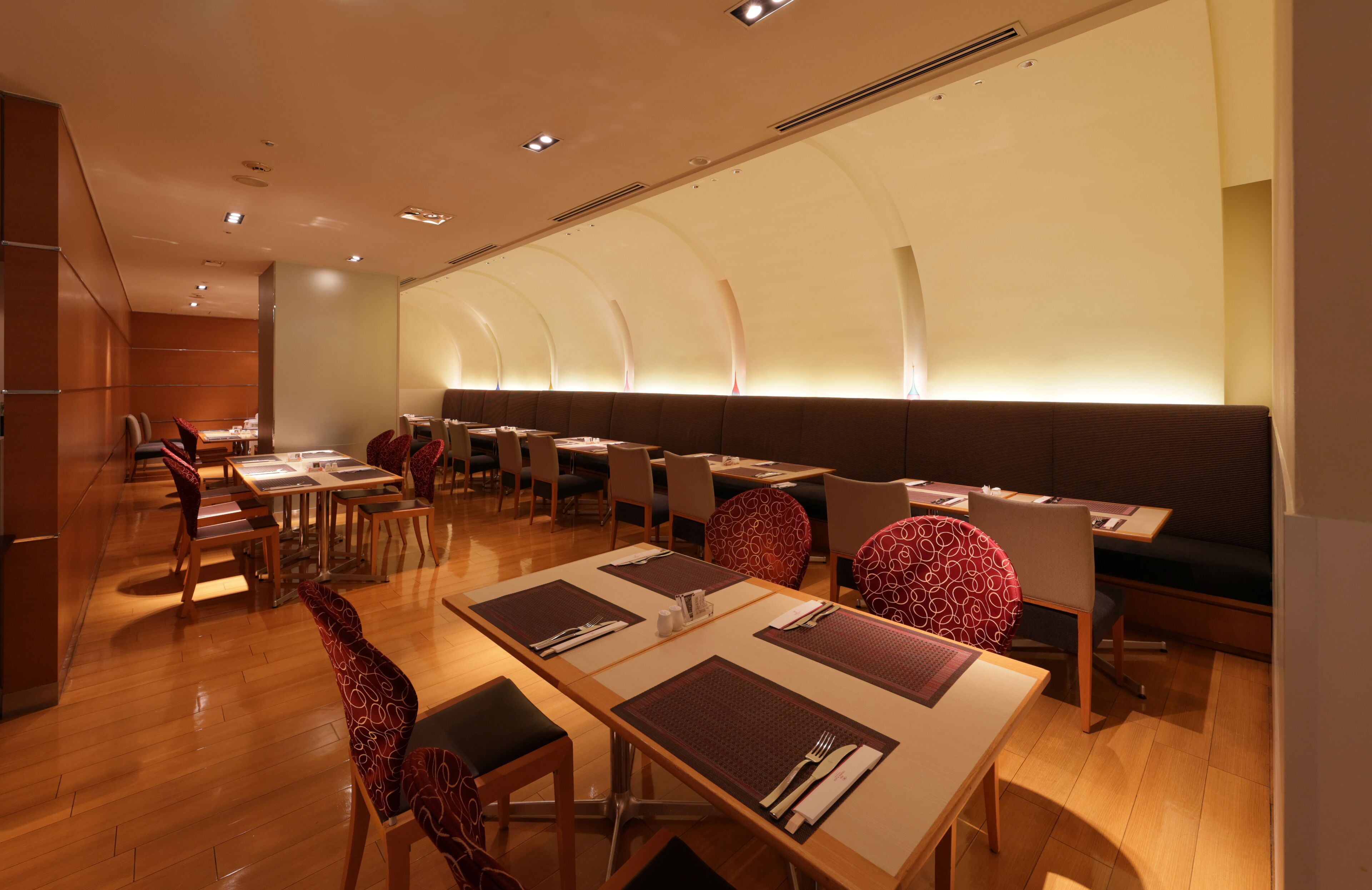 A restaurant with wooden tables and chairs, a long counter, and a high ceiling with recessed lighting.