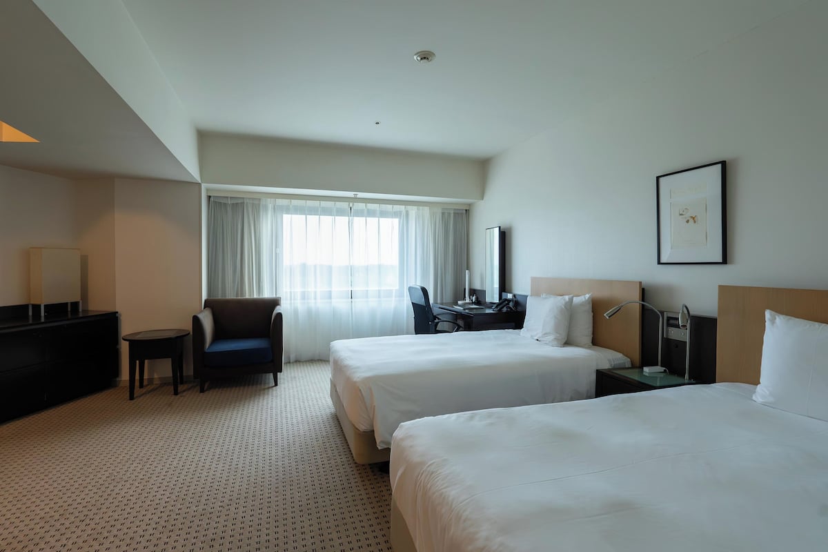A hotel room with two beds, a desk, a chair, a TV, and a window with curtains.
