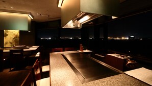 Een modern restaurant met een lange balie, zitplaatsen en uitzicht over de stad 's nachts.