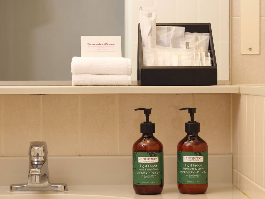 A bathroom with a sink, two bottles of hand and body wash, a towel, and a card on the shelf.