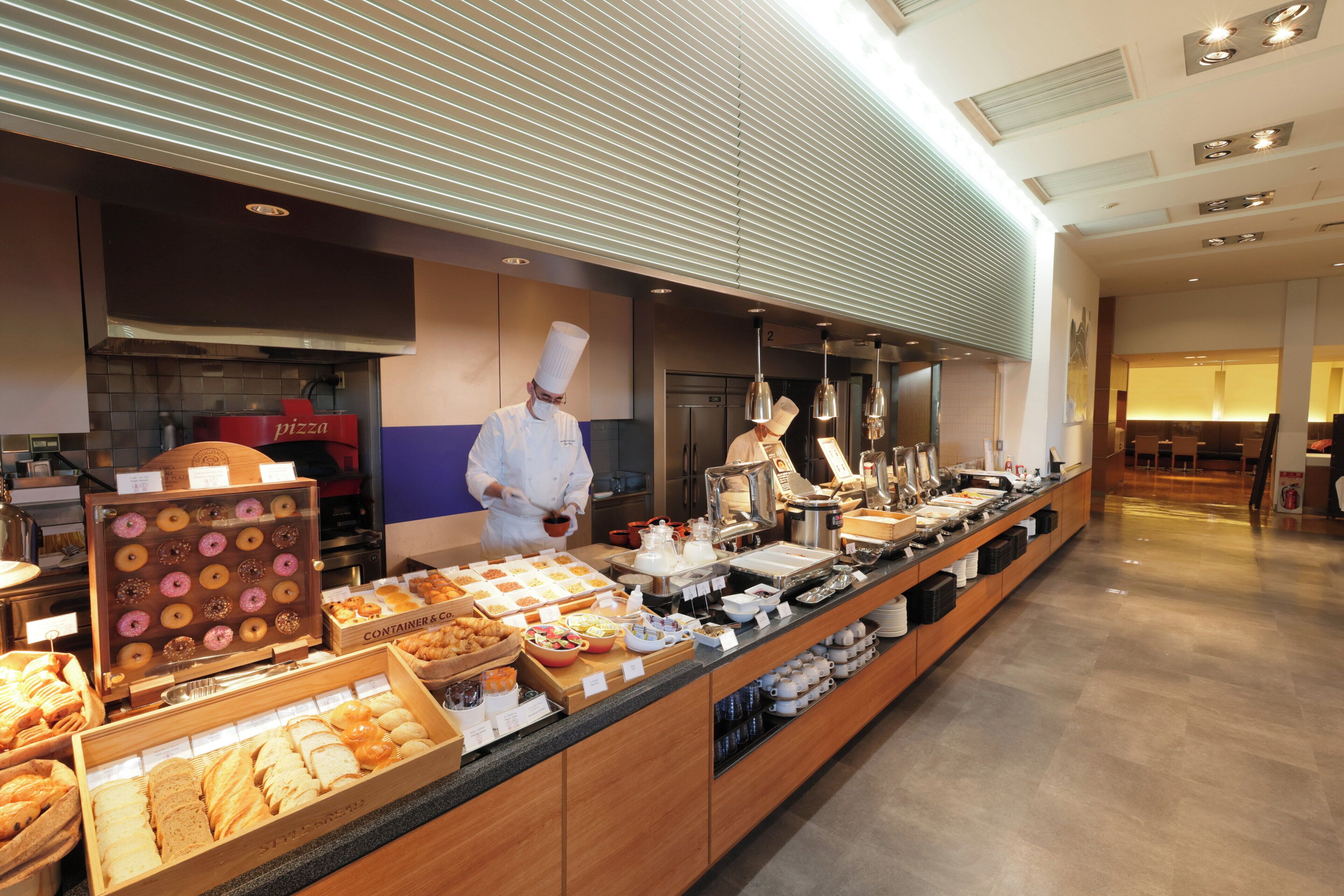 A buffet area with a variety of food options including pastries, bread, and a pizza station.