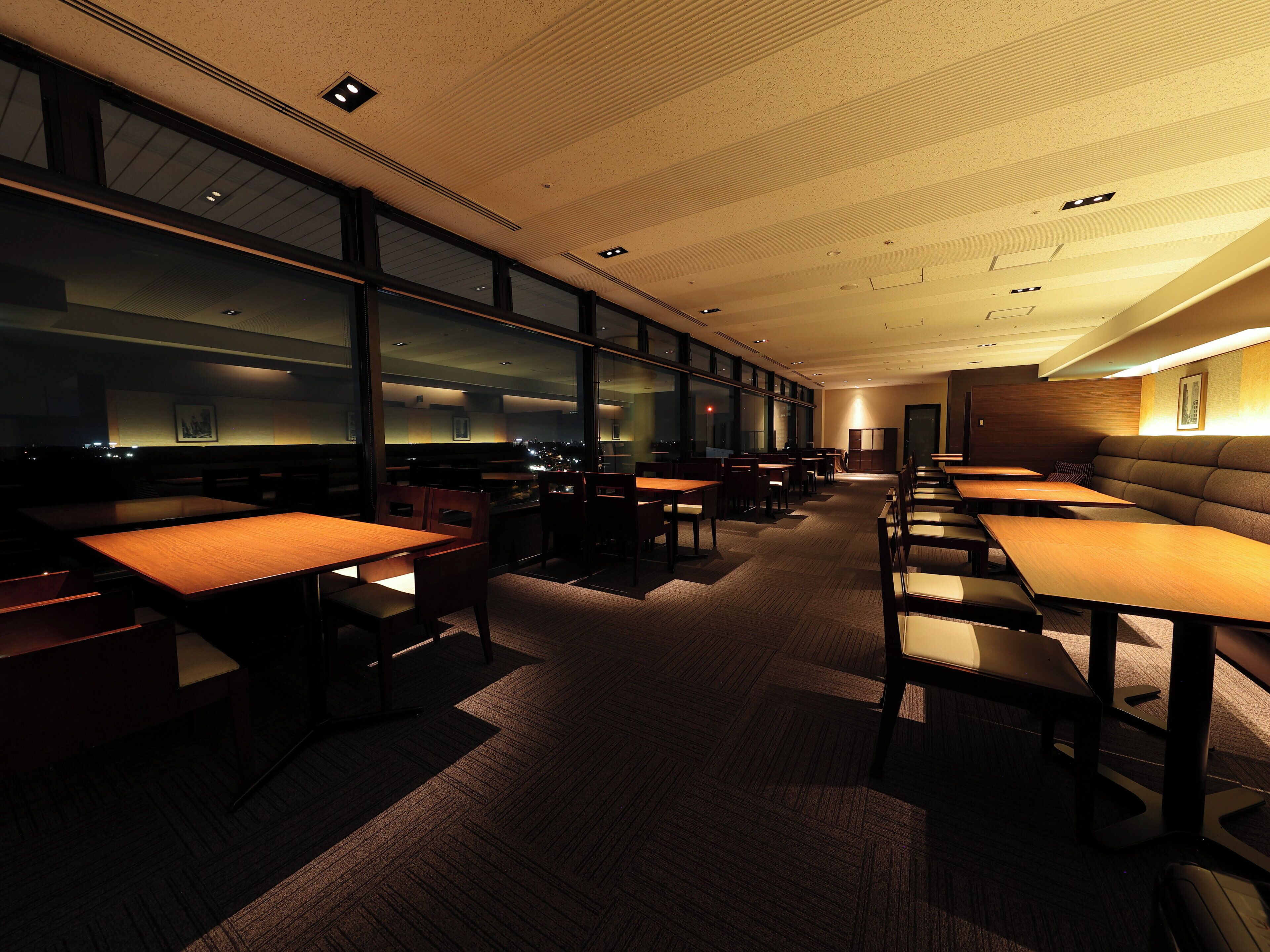 A modern dining area with tables and booths, large windows, and a view of the city at night.