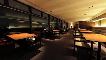 A modern dining area with tables and booths, large windows, and a view of the city at night.