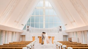 Een kerkinterieur met houten banken, een groot kruis en een stel bij het altaar.