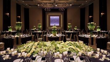 A banquet hall with round tables set for a formal event, featuring floral centerpieces and candlelit tables.