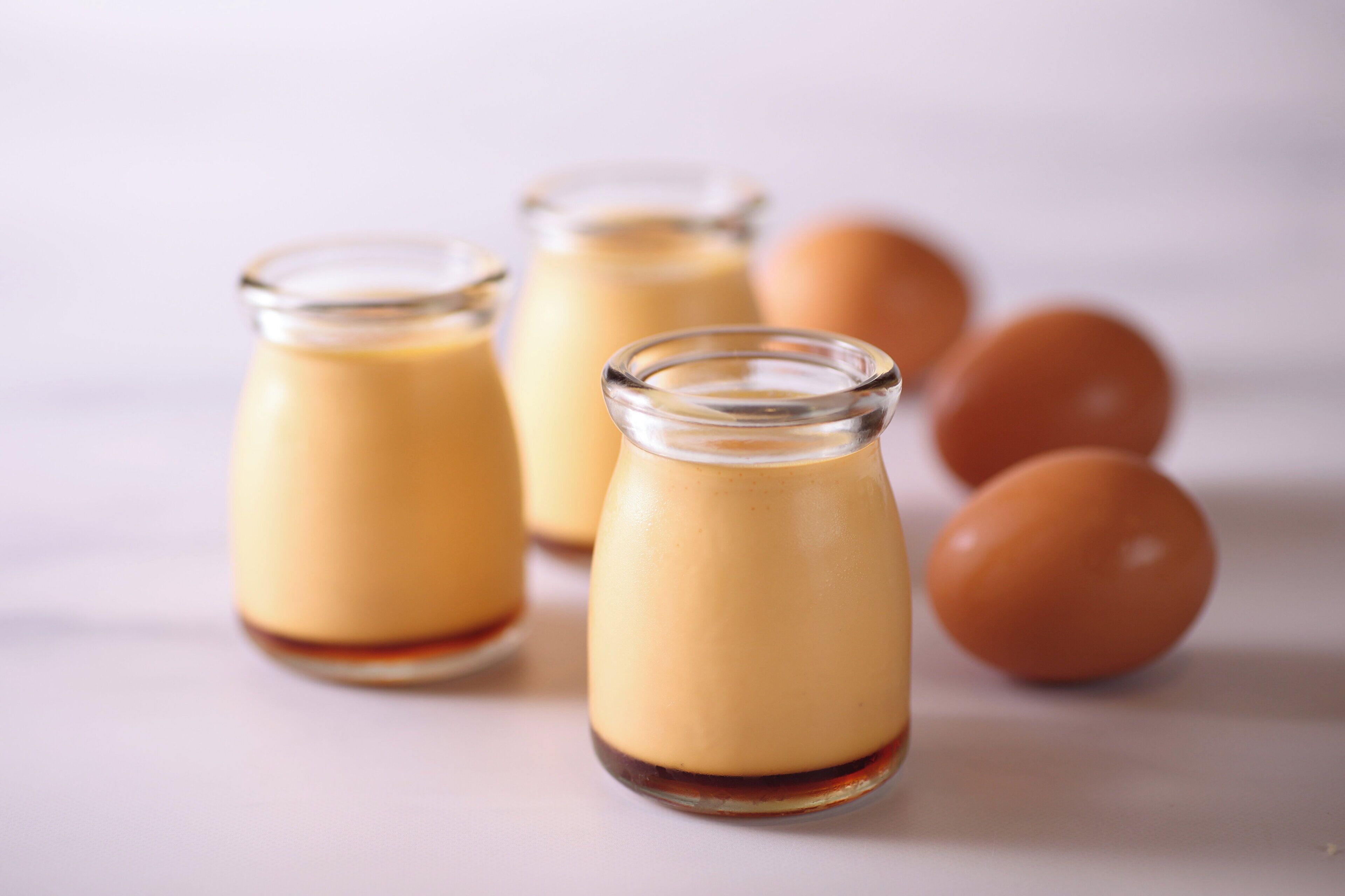 Trois bocaux en verre contenant une substance crémeuse, qui pourrait être un dessert, et trois œufs au fond.