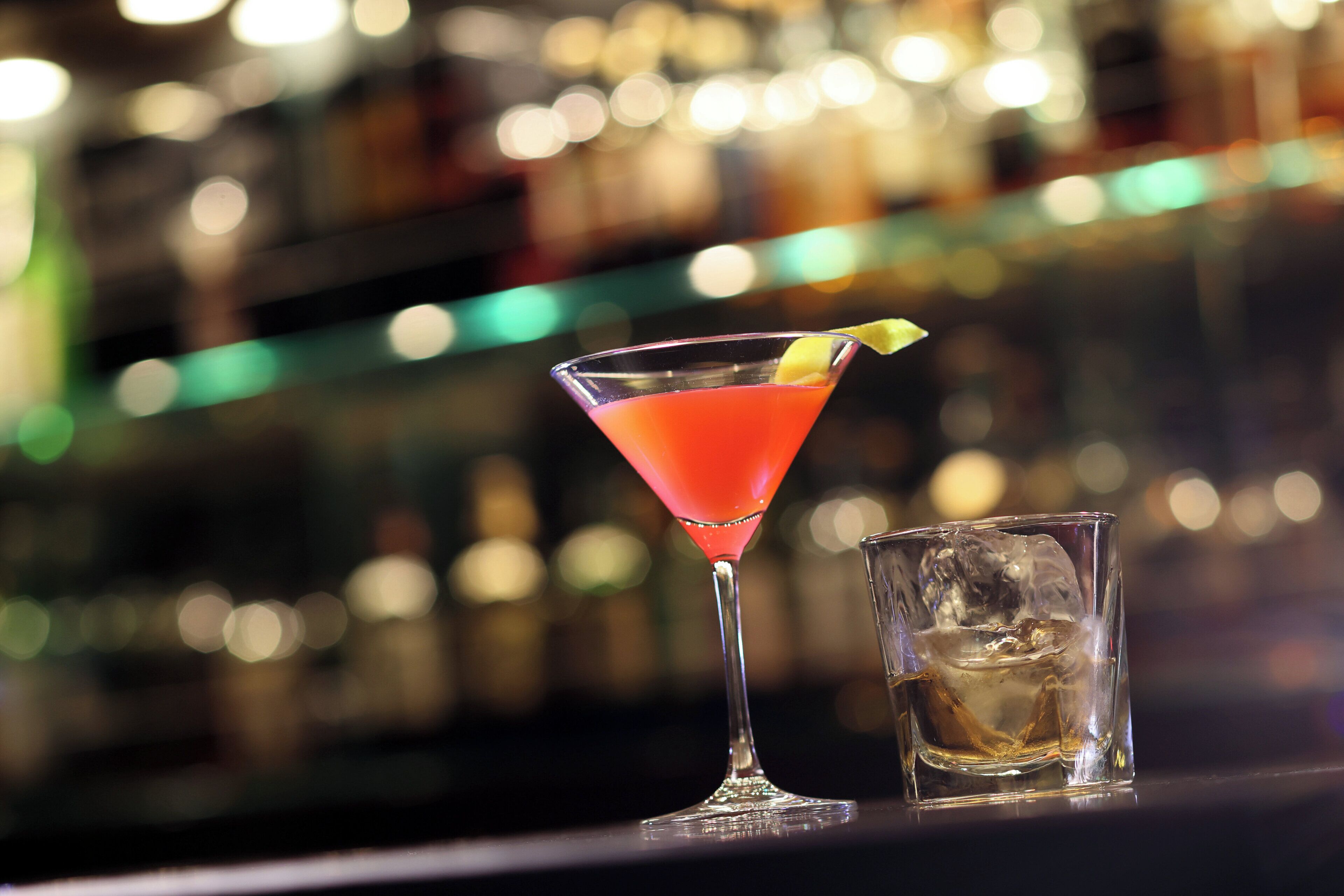Una copa de martini con una bebida roja y un giro de limón sobre una barra.