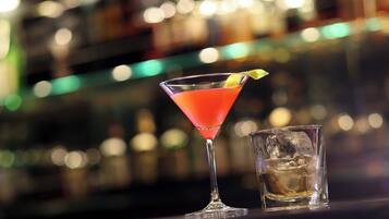 Una copa de martini con una bebida roja y un giro de limón sobre una barra.