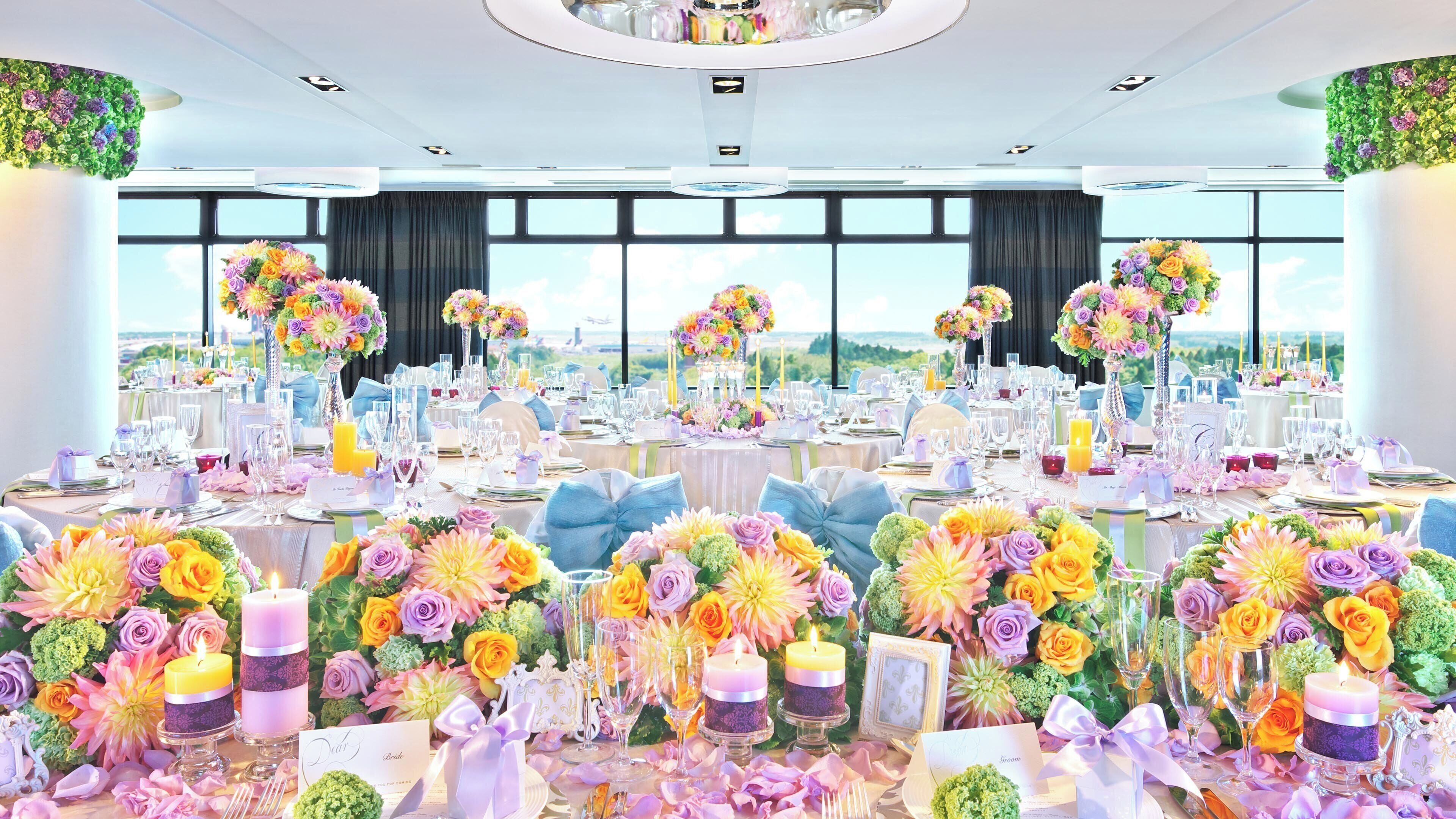 Un salón de banquetes con mesas redondas, centros de mesa florales y vistas amplias a través de grandes ventanales.