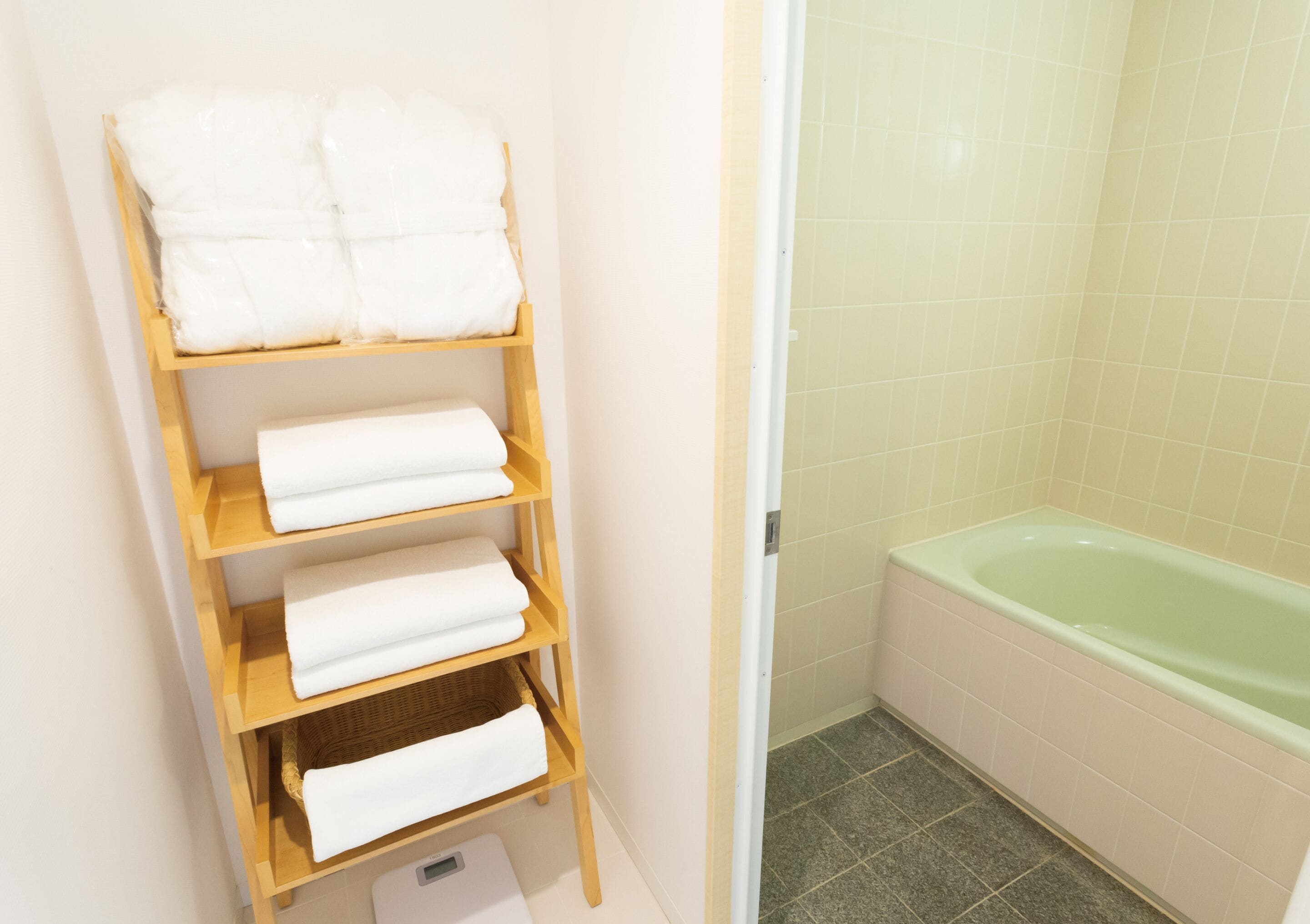 A bathroom with a wooden shelf holding white towels, a green bathtub, and tiled walls.