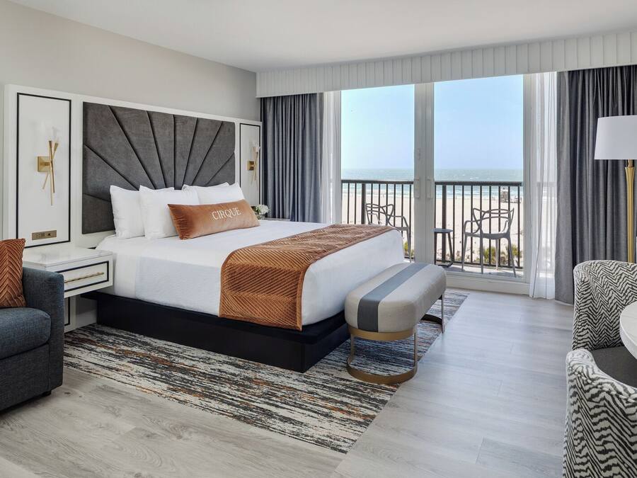 Una camera d'albergo moderna con un letto grande, un balcone con vista e un'area salotto con un tavolo.