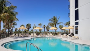 A swimming pool with lounge chairs and umbrellas, surrounded by palm trees and a clear blue sky. - Cirque St. Armands Beachside (Sarasota)