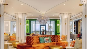 A modern hotel lobby with a curved orange sofa, green walls, and a large chandelier. - Cirque St. Armands Beachside (Sarasota)