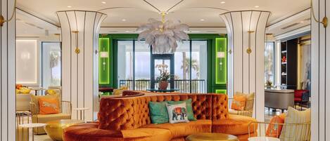 En moderne hotellobby med en buet orangefarvet sofa, grønne vægge og en stor lysekrone.
