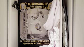A closet with a poster of Barnum & Bailey Greatest Show on Earth, a bench, and hanging clothes.