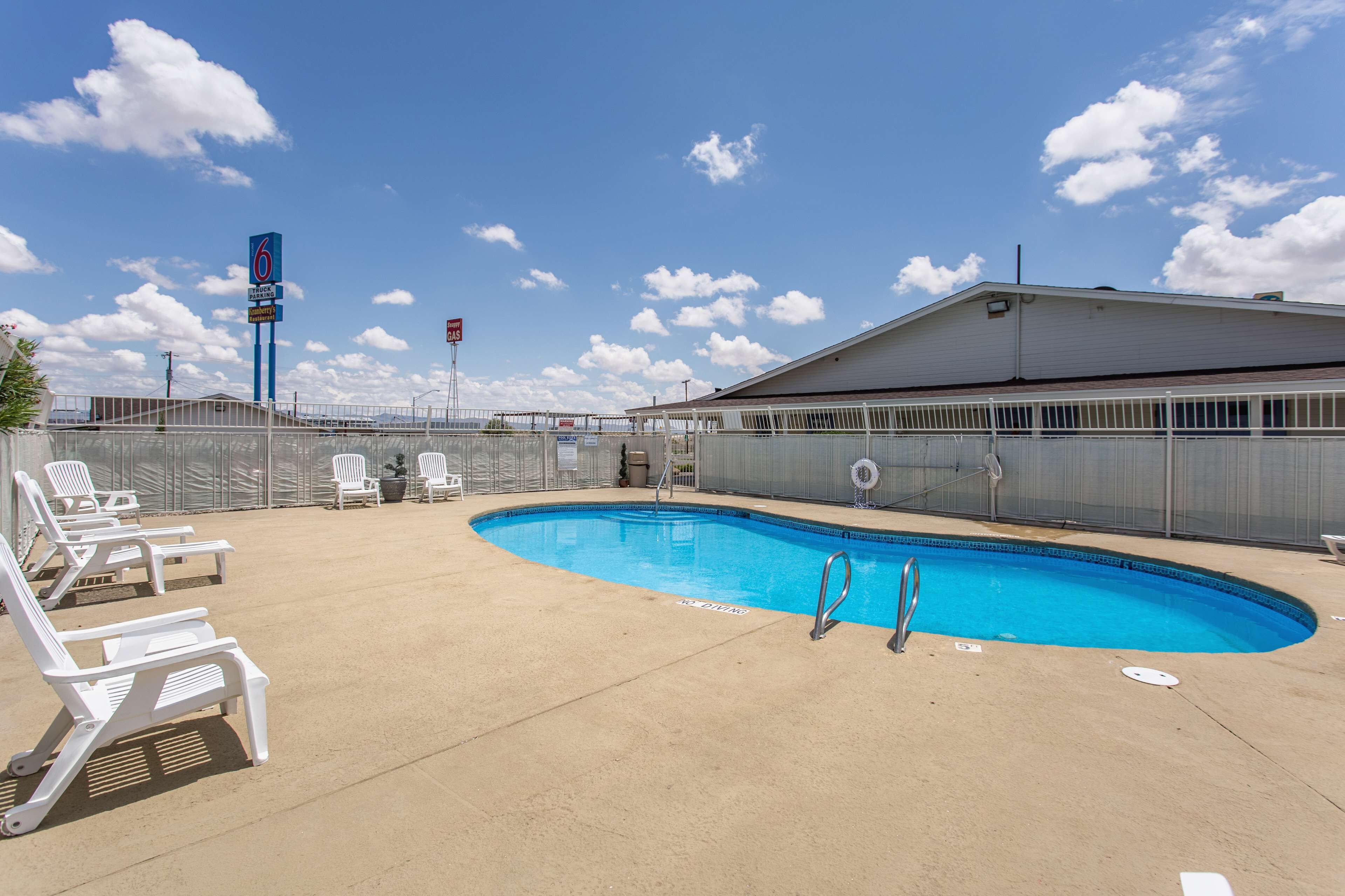 A swimming pool with lounge chairs, a fenced area, and a building in the background.