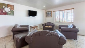 A living room with leather sofas, a flat-screen TV, a small table, and a window with blinds. - Motel 6 Lordsburg, NM (Lordsburg)