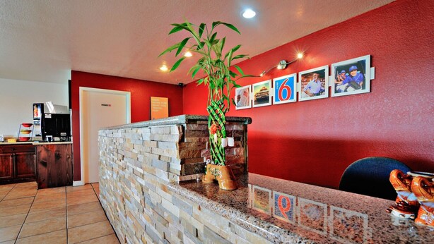 A reception area with a stone wall, a potted plant, and a counter with a coffee machine. - Motel 6 Lordsburg, NM (Lordsburg)