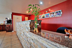 A reception area with a stone wall, a potted plant, and a counter with a coffee machine. - Motel 6 Lordsburg, NM (Lordsburg)