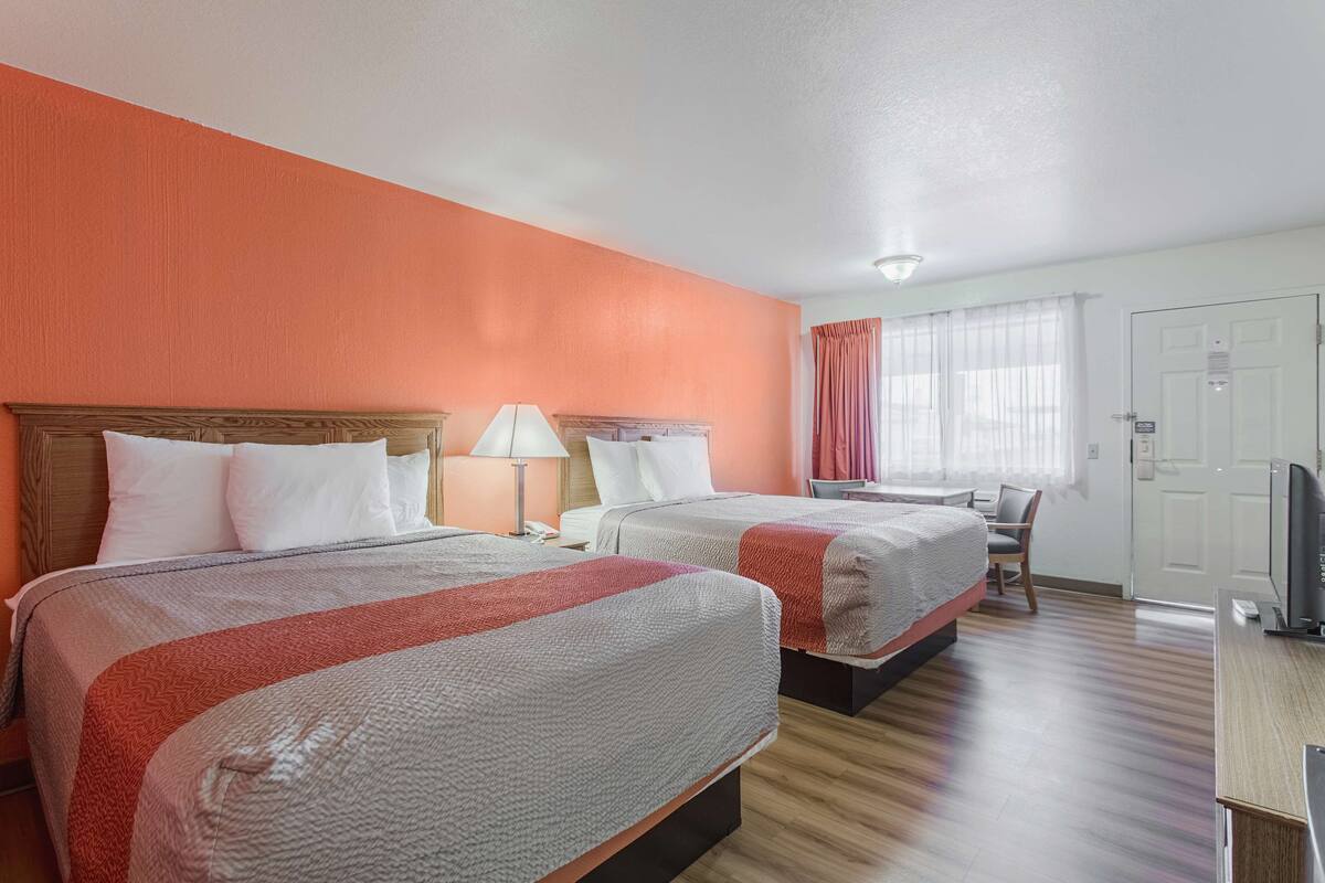 A hotel room with two beds, a desk, a chair, a television, and a window with curtains.