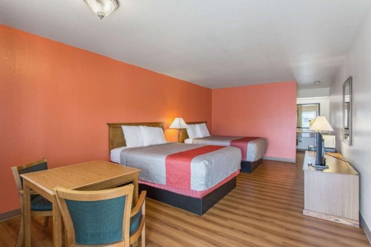 A hotel room with two beds, a wooden desk, and a chair.