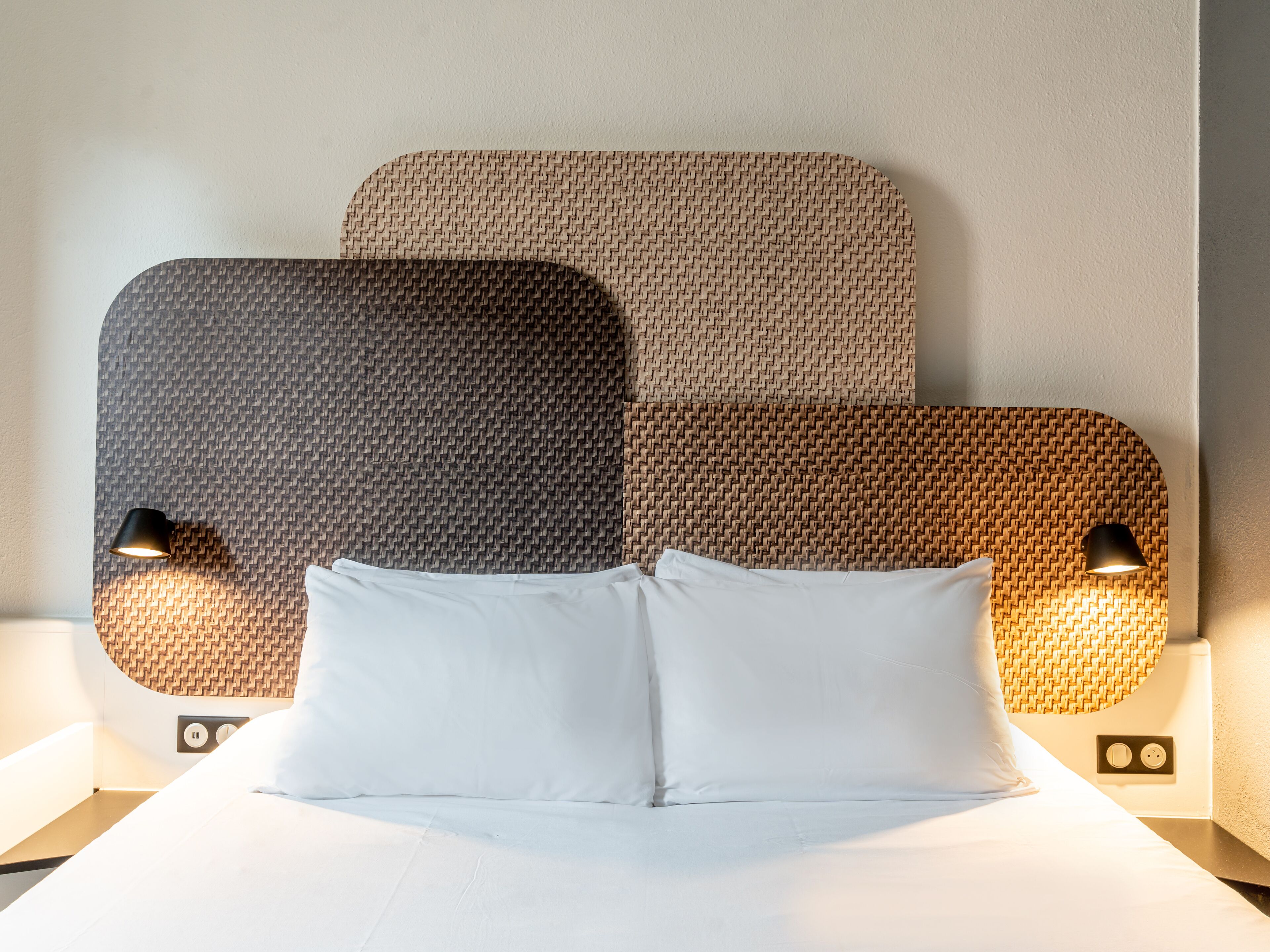 Habitación de hotel con una cama, dos lámparas fijadas a la pared y un panel de pared con textura.