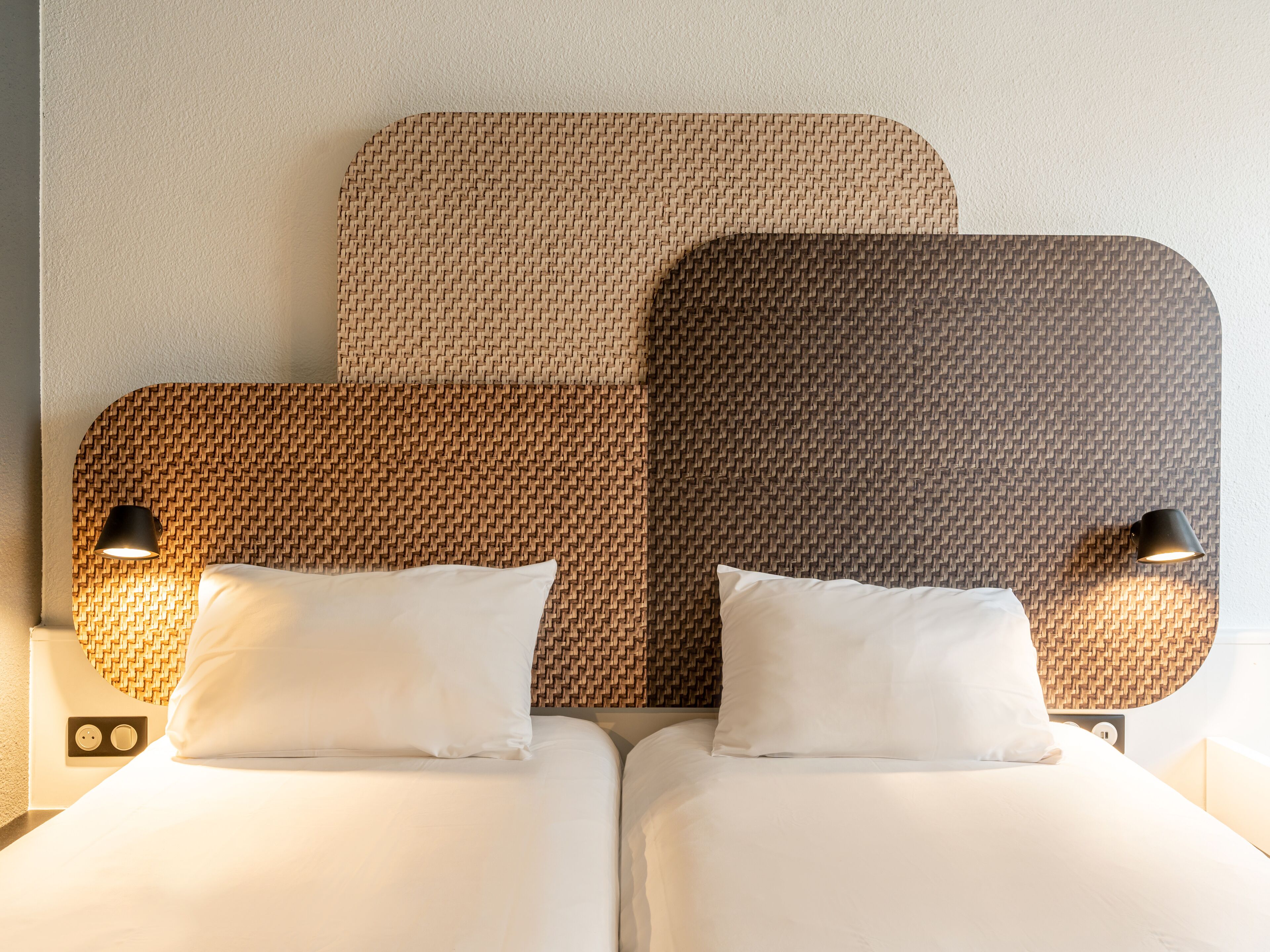 A double bed with a woven headboard and two bedside lamps.