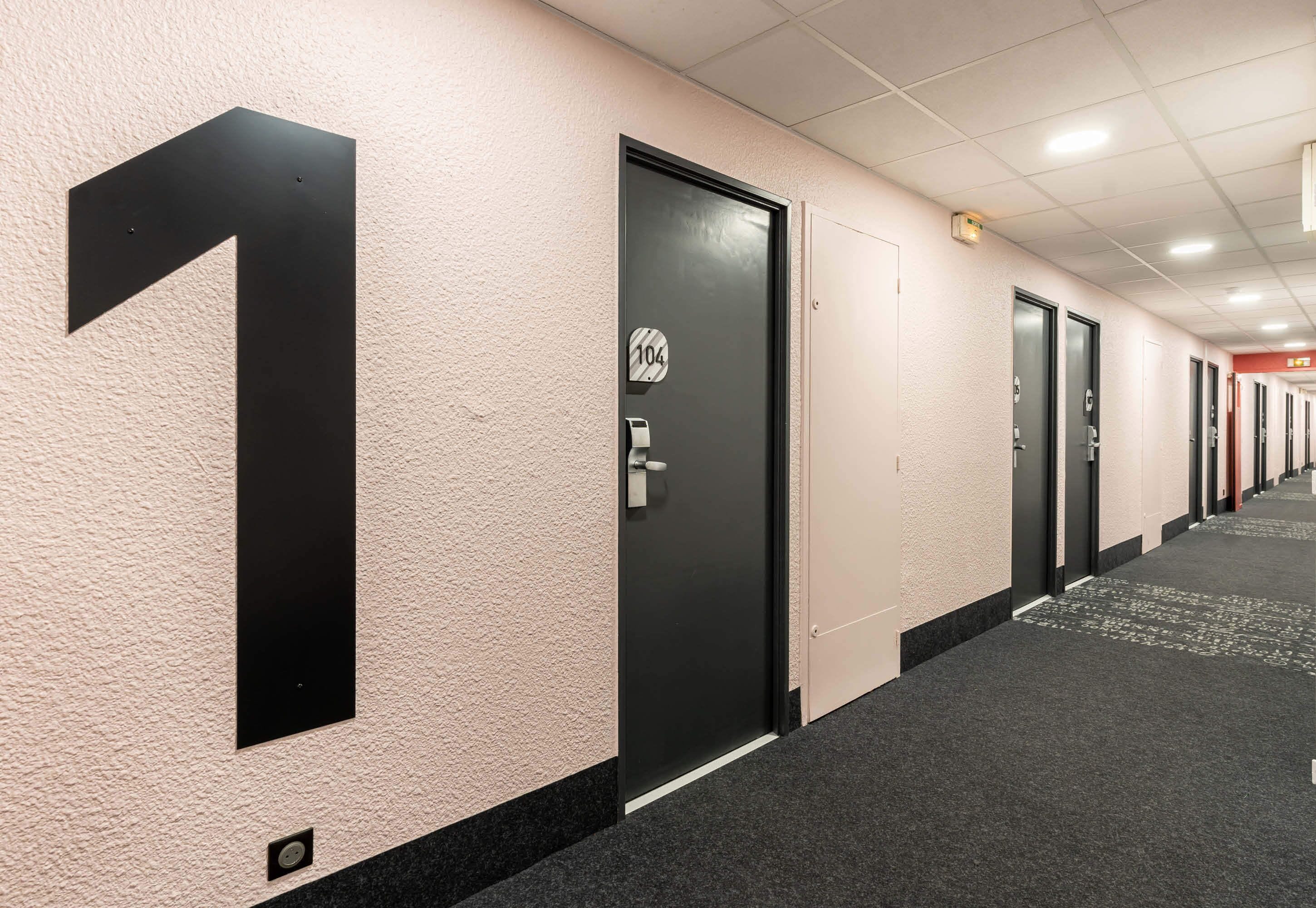 Un pasillo de hotel con puertas numeradas, pisos alfombrados y pared con textura.