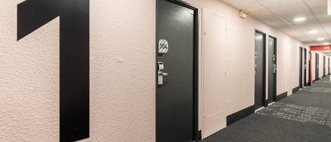 Un couloir d’hôtel avec des portes numérotées, un sol recouvert de moquette et un mur à texture.