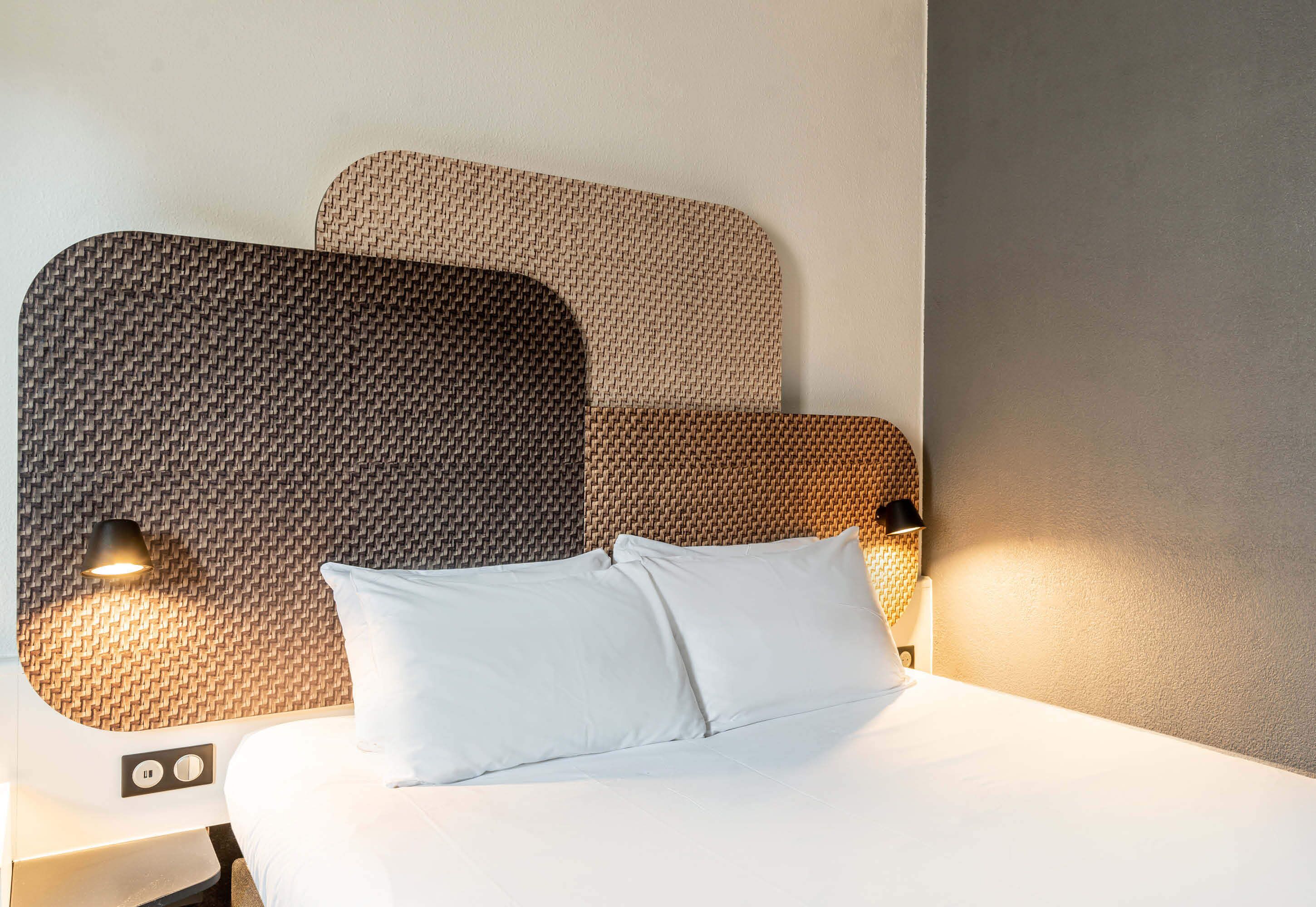 A neatly made bed with white linens and two pillows, a headboard with a woven pattern, and two bedside lamps.