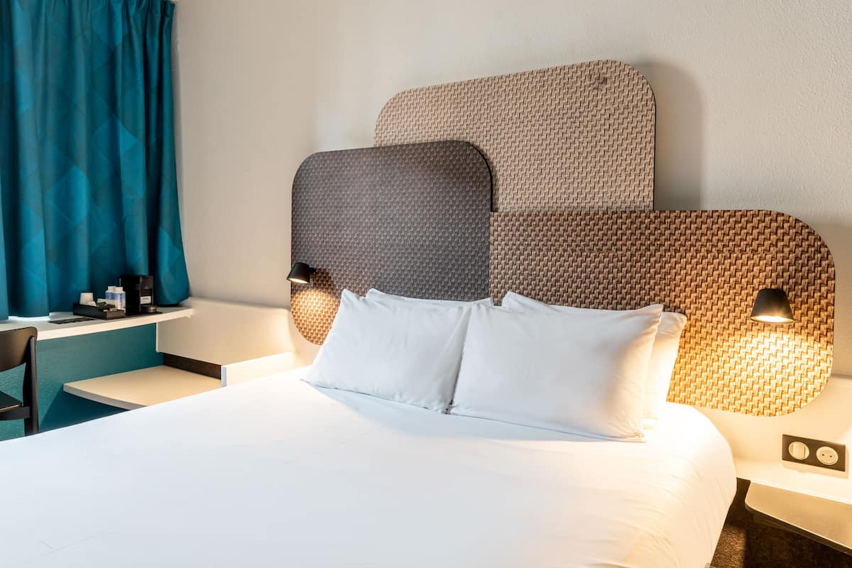 Une chambre d’hôtel avec un grand lit, un bureau avec une chaise, une machine à café et une lampe.