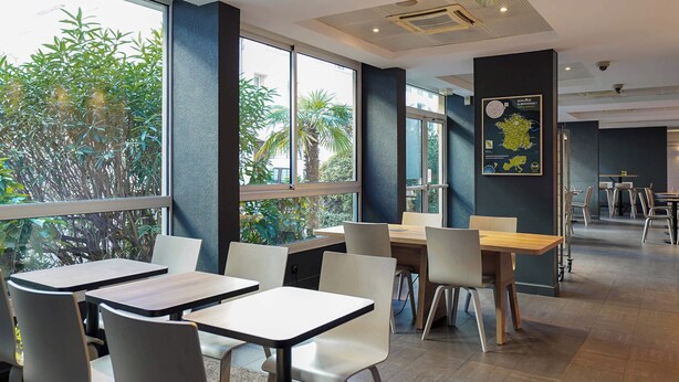 Un restaurant moderne avec de grandes fenêtres, des chaises blanches et des tables en bois.