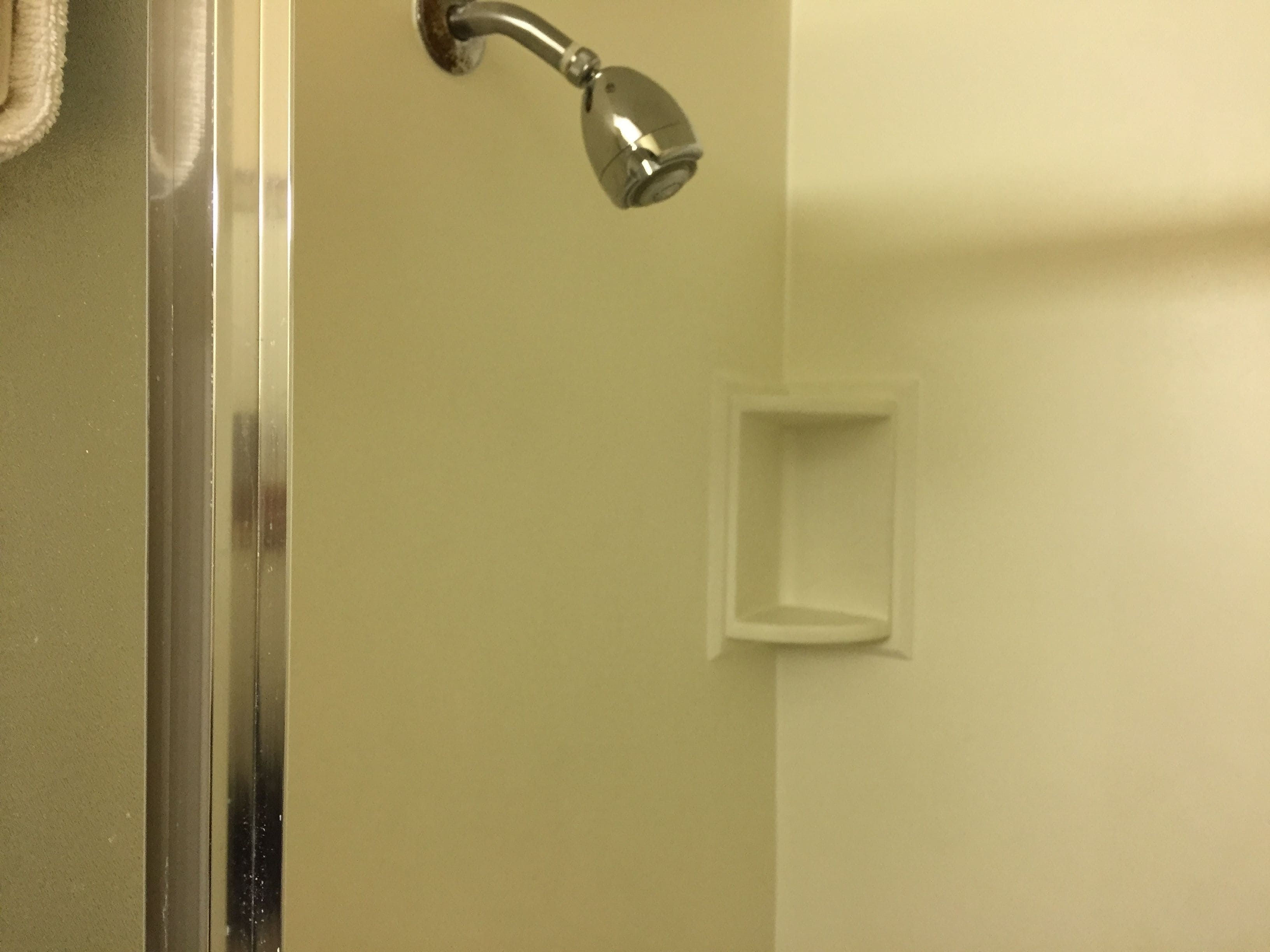 Un bagno con doccia, porta in vetro e piccolo ripiano bianco.