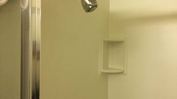 Un bagno con doccia, porta in vetro e piccolo ripiano bianco.