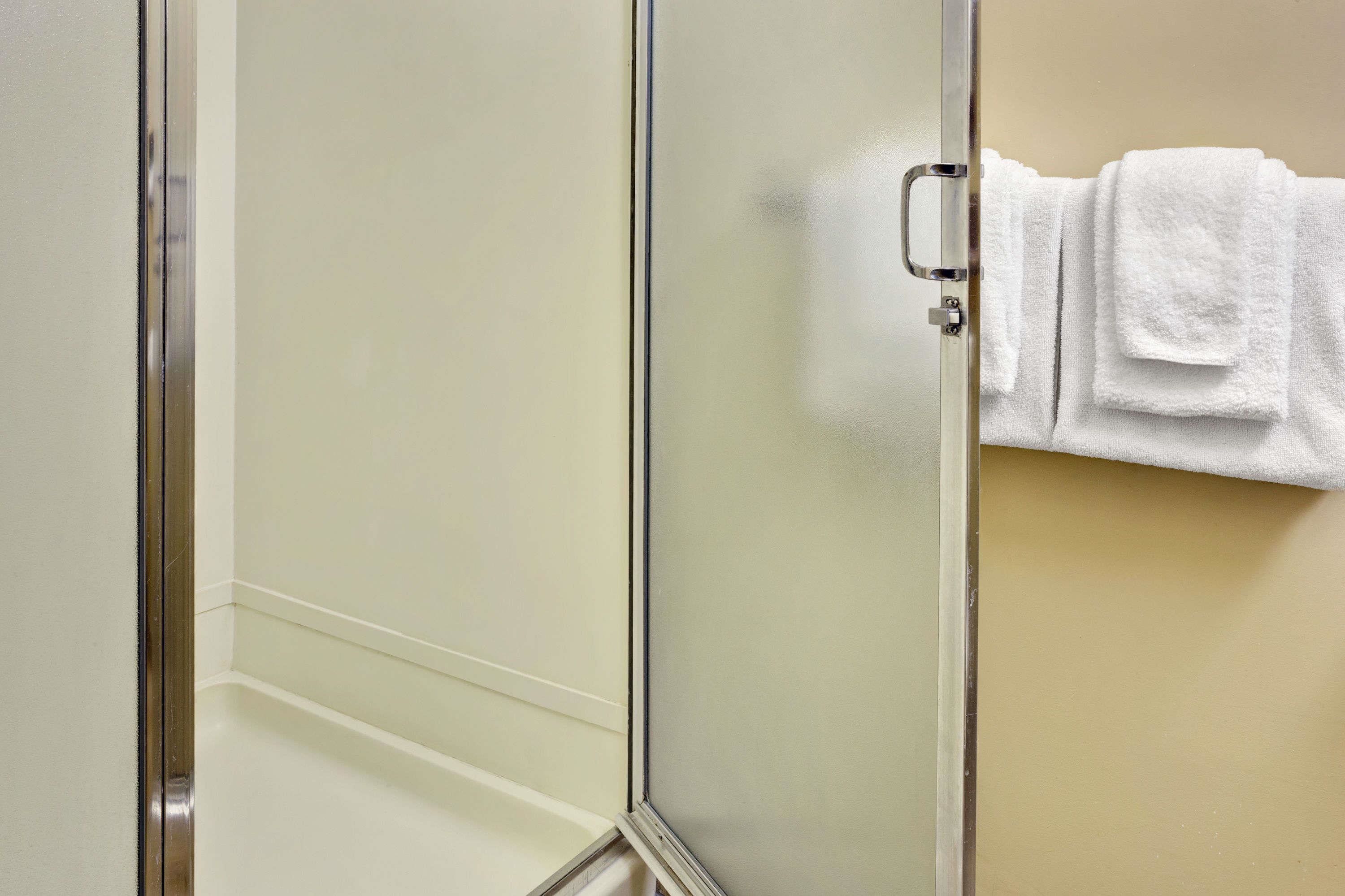 A bathroom with a glass shower door, a white towel hanging on the wall, and a beige wall.