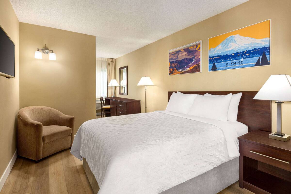 Hotelkamer met een groot bed, een bruine fauteuil, een bureau en twee wandlampen. Op de muur hangen twee foto's, één met een berg en de andere van de Olympische Spelen.