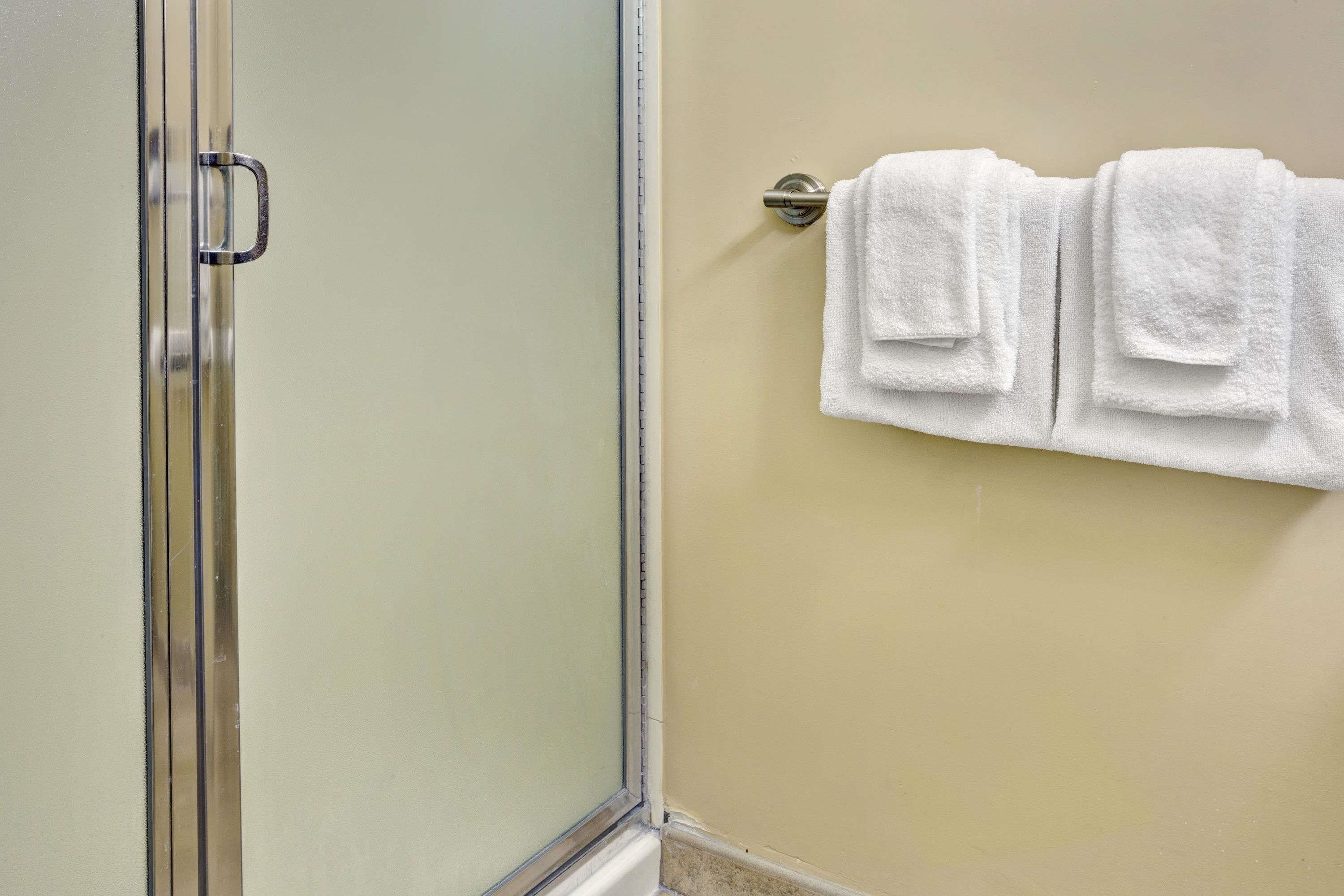 A bathroom with a glass shower door, a towel rack with three white towels, and a beige wall.