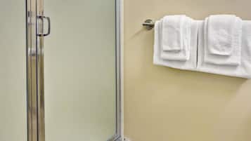 A bathroom with a glass shower door, a towel rack with three white towels, and a beige wall.