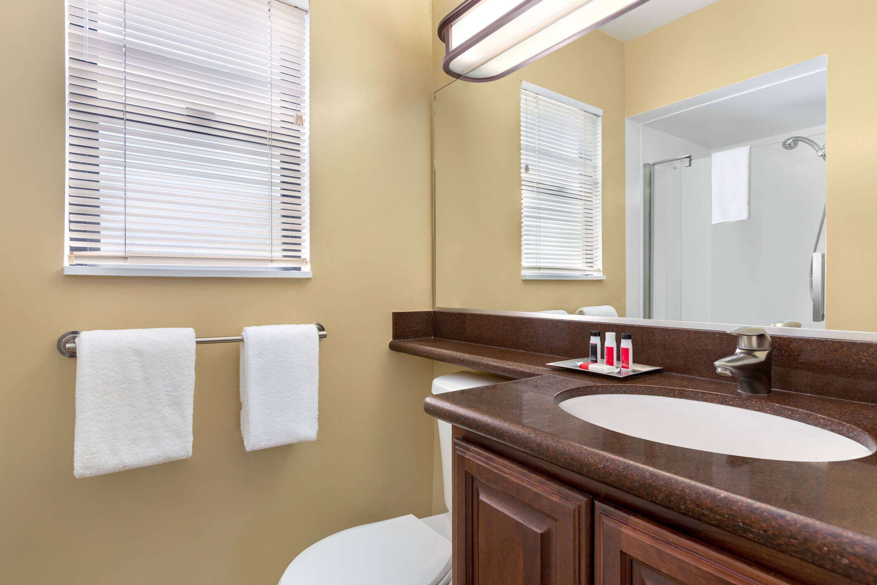 A bathroom with a sink, mirror, towel rack, and a shower area.