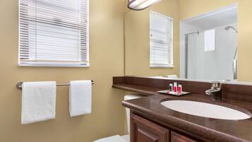 A bathroom with a sink, mirror, towel rack, and a shower area.