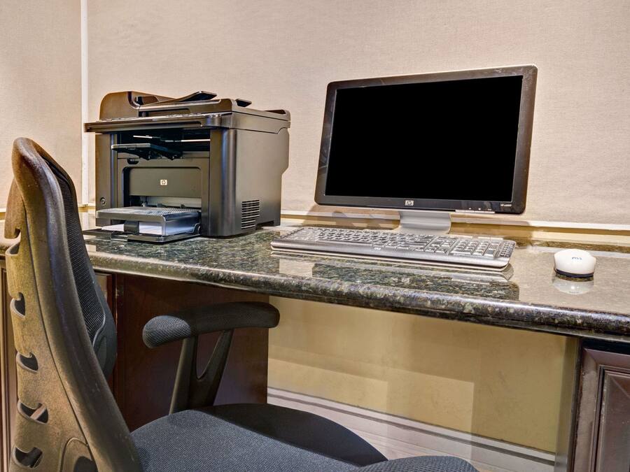 Ein Arbeitsplatz im Hotel mit einem Schreibtischcomputer, einem Drucker und einem Stuhl.