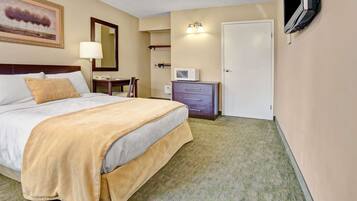 A hotel room with a large bed, a bedside table, a lamp, a TV, and a door.