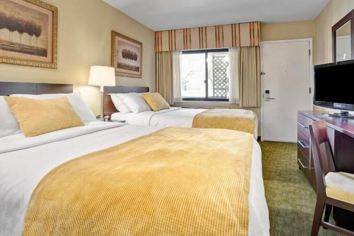 A hotel room with two beds, a desk, a TV, and artwork on the walls.