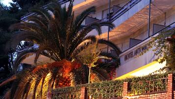 A hotel with a palm tree in front, a brick wall with greenery, and a balcony with a railing.